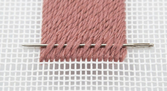Close-up of needlepoint canvas mesh with a needle woven under flat stitches on the back