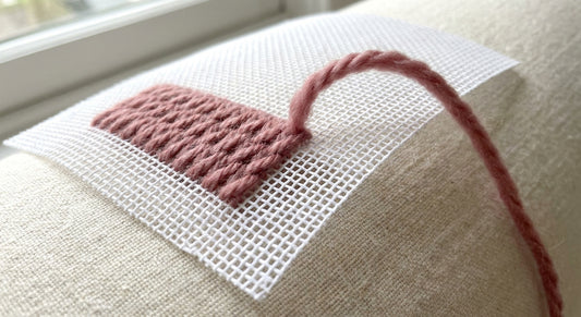 Relaxed strand of wool rising from evenly tensioned stitches on flat needlepoint canvas