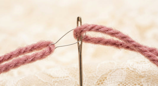 Needle threader wire loop pulling dusty rose wool through a tapestry needle eye