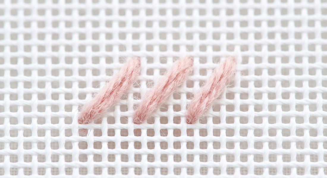 Three tent stitches in blush pink wool on white needlepoint canvas — the one stitch beginners need
