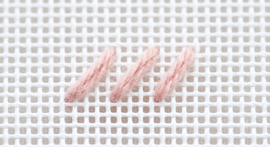 Three tent stitches in blush pink wool on white needlepoint canvas — the one stitch beginners need