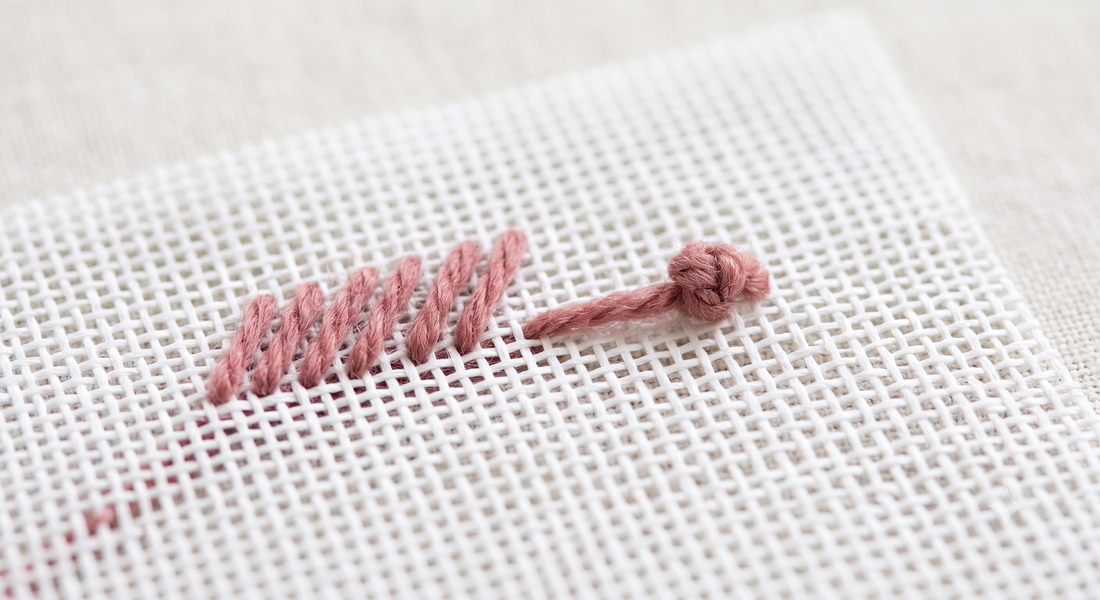 Waste knot technique on needlepoint canvas — knot on the surface ahead of a row of dusty rose tent stitches