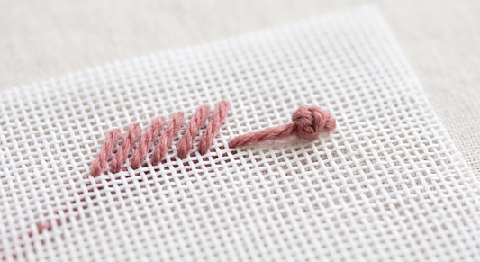 Waste knot technique on needlepoint canvas — knot on the surface ahead of a row of dusty rose tent stitches