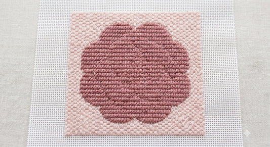 Stitched rose flower popping forward from a subtler textured needlepoint background